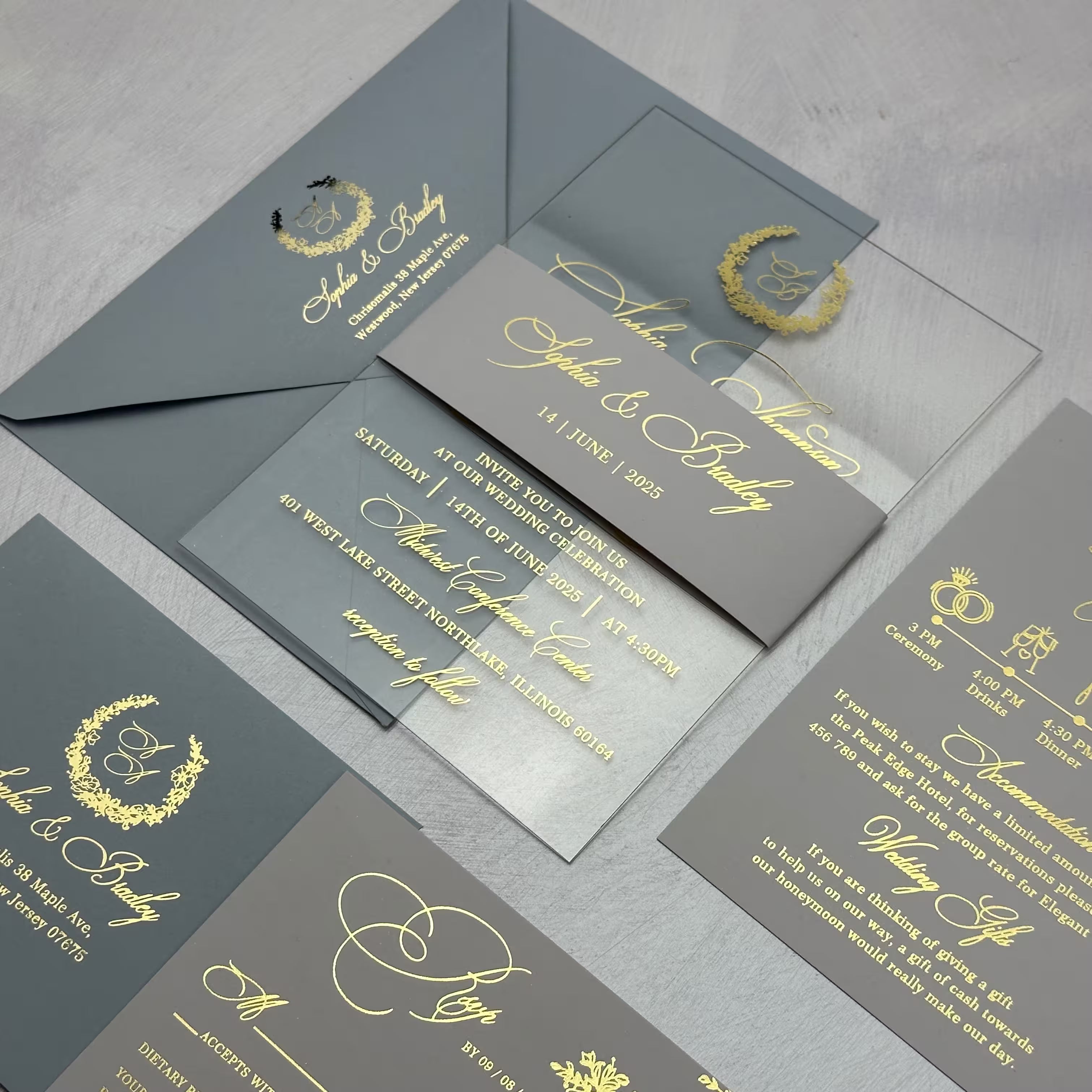 Acrylic wedding invitation suite with a monogram wreath in gold foil, wrapped in a printed belly band with the couple's names and date beside a details card and RSVP