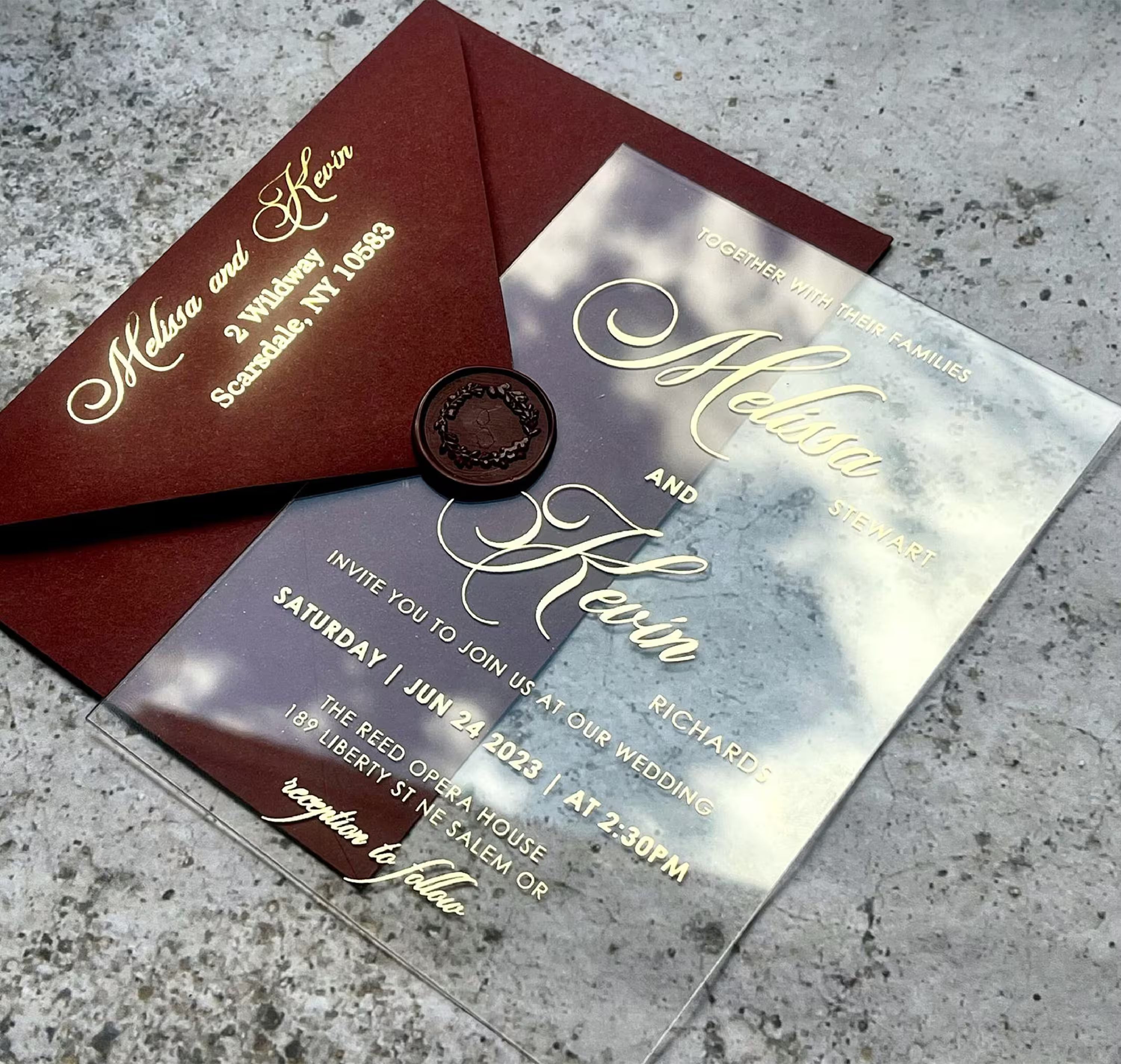Burgundy acrylic wedding invitation suite flat lay with the clear invitation, foiled belly band, RSVP and details card and a matching burgundy envelope