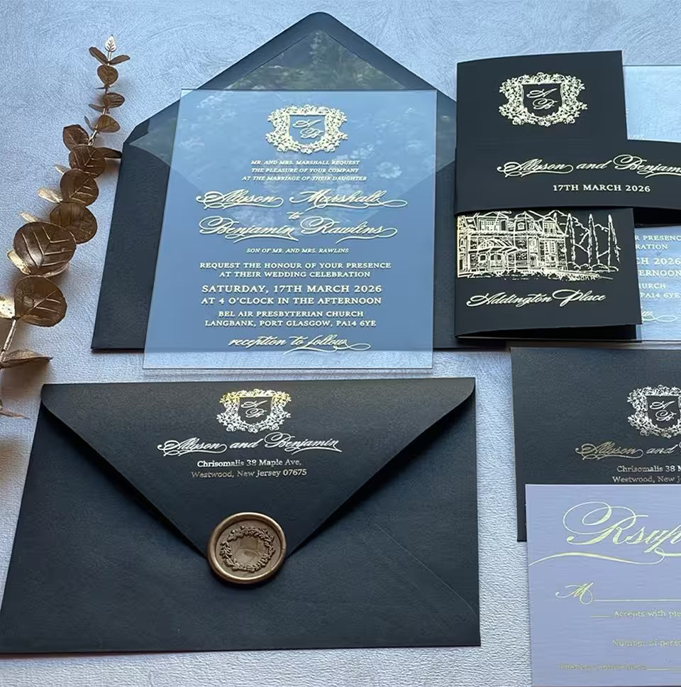Clear acrylic wedding invitation with a gold foil monogram crest above the couple's names in calligraphy