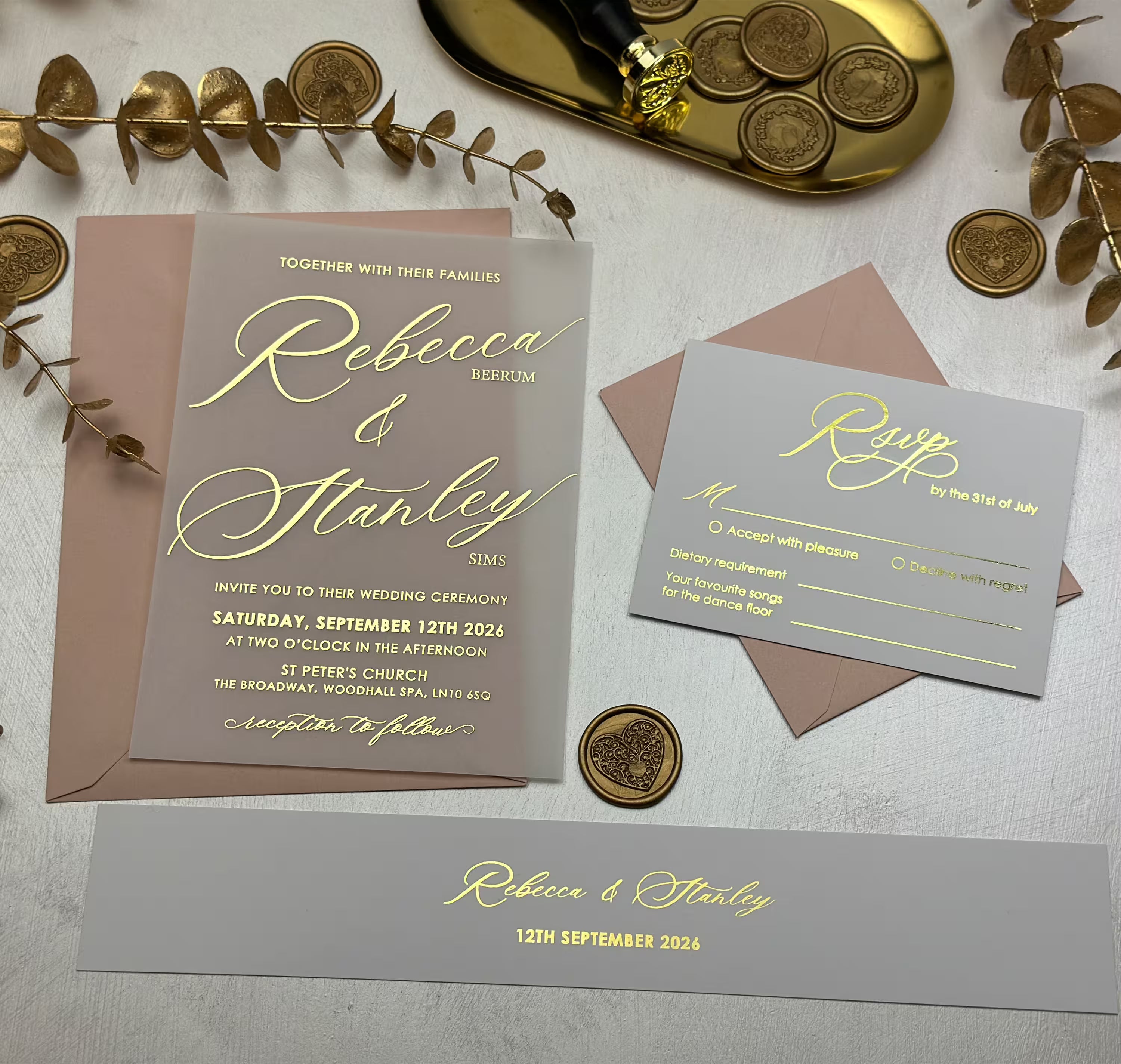 Flat lay of a vellum paper wedding invitation suite with gold foil, grey cards and a blush envelope