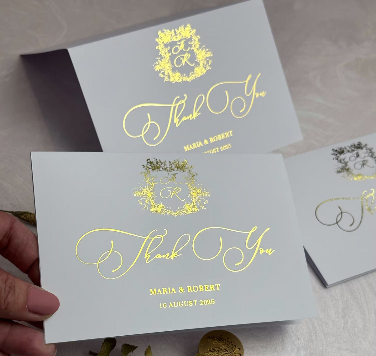 Wedding thank you notes with flowing foil script and floral crest monogram, held in hand