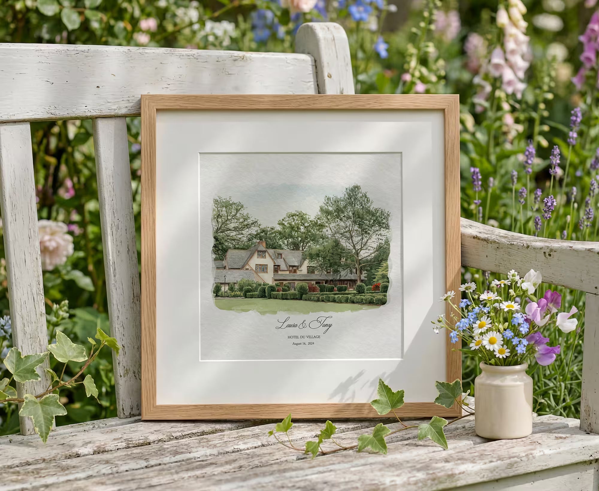 Framed watercolor wedding venue portrait with couple names, displayed in a garden as an anniversary gift