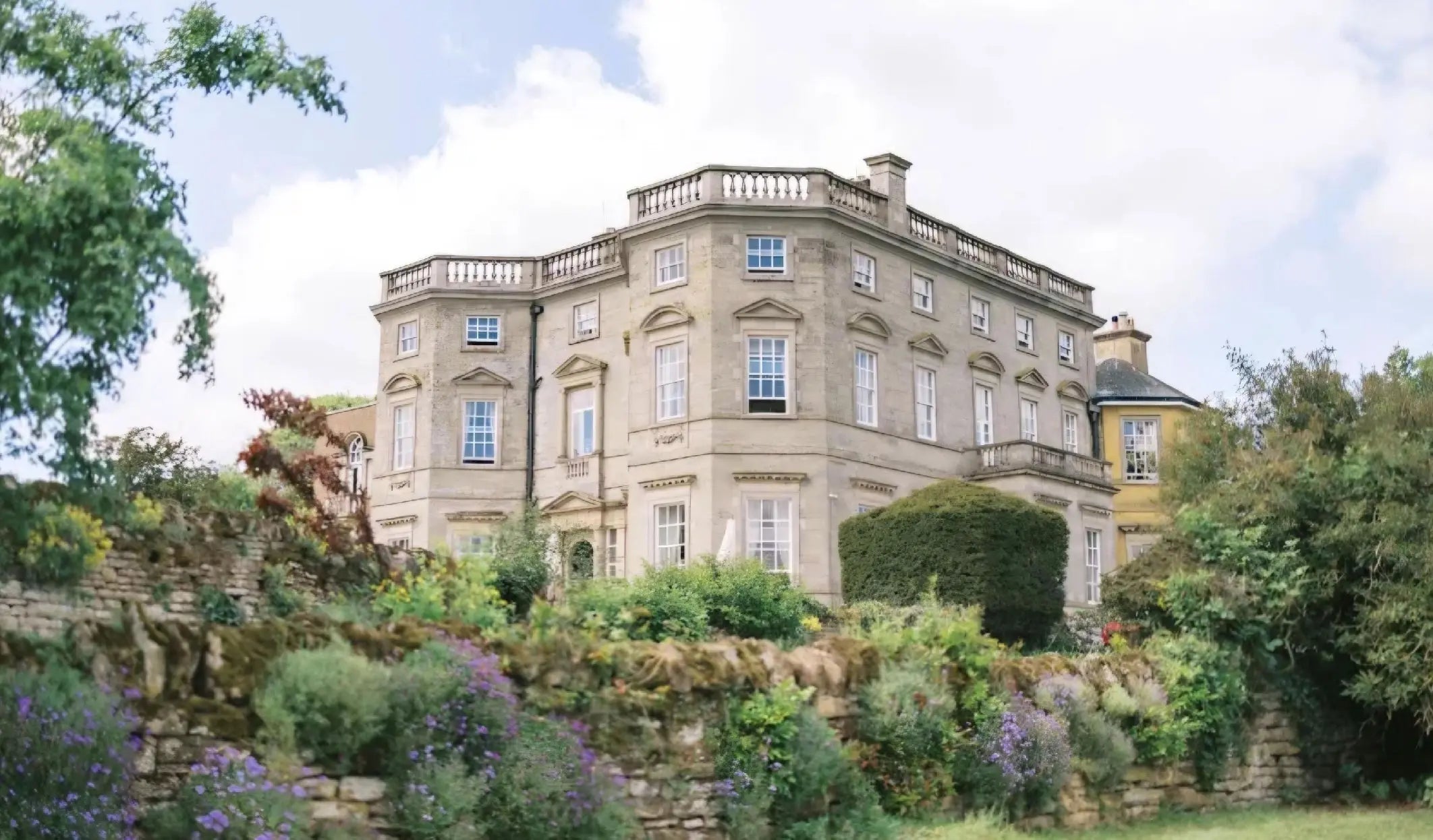 Elegant original photograph of Bourton Hall wedding venue surrounded by garden landscaping and historic stone walls in the English countryside.