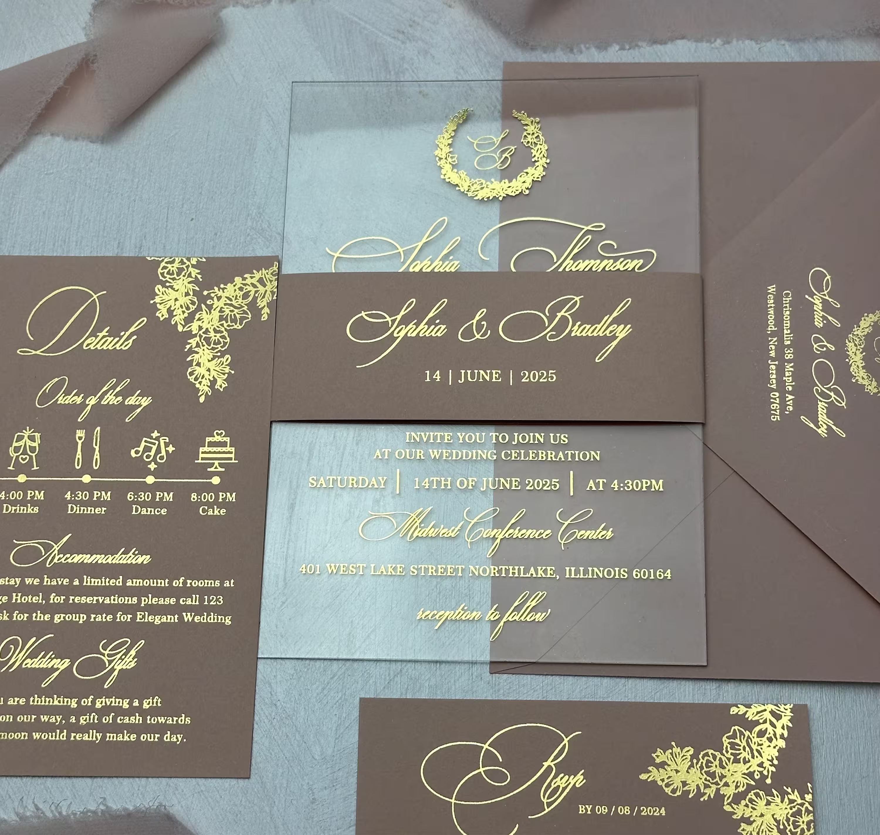 Clear acrylic wedding invitation with a gold foil monogram wreath and calligraphy names, shown with a burgundy envelope, matching details card, RSVP and belly band as a full personalized suite