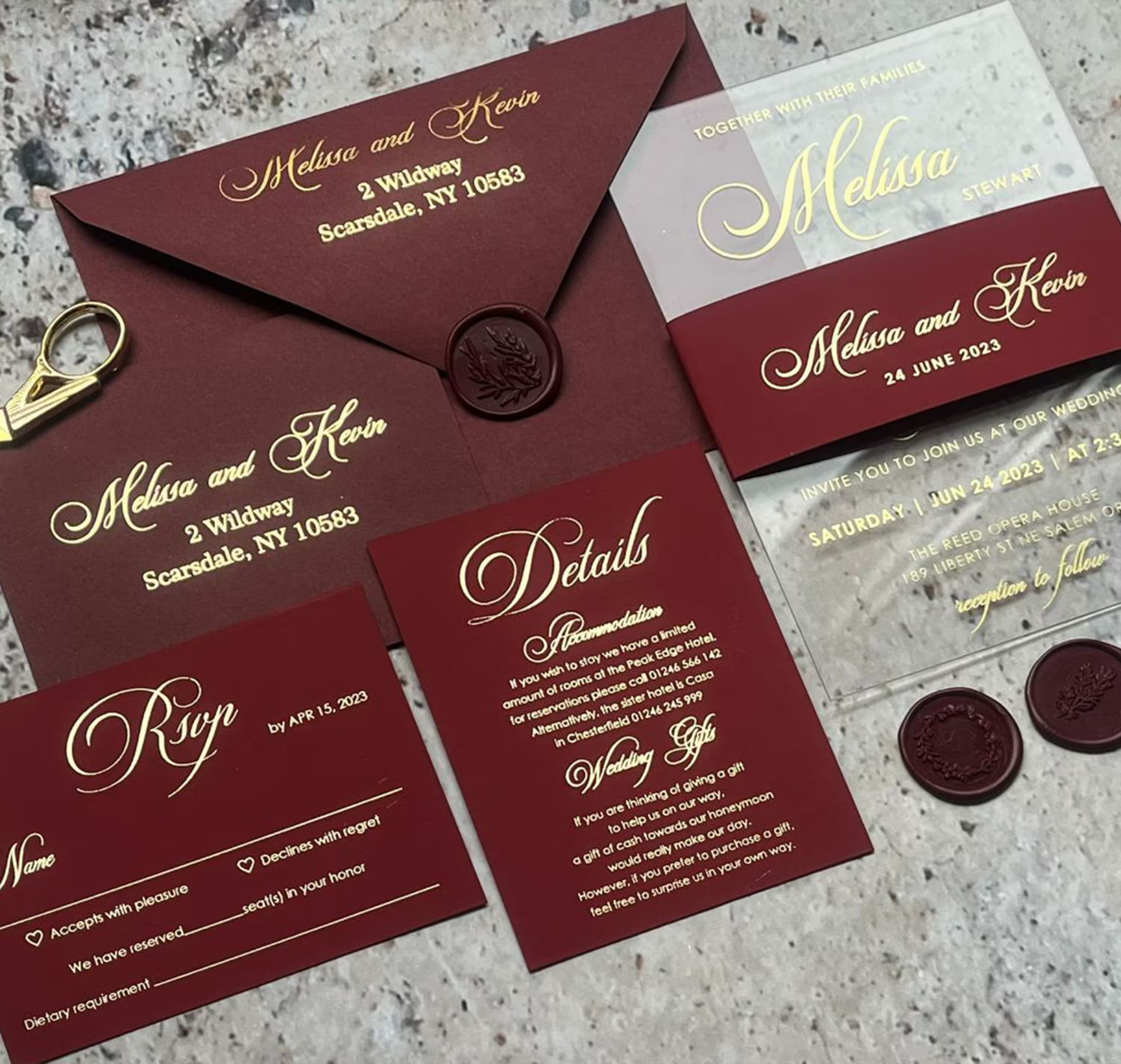 Clear acrylic wedding invitation with gold foil names in formal script, paired with a deep burgundy envelope addressed to the couple