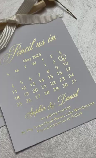 Video of a pencil us in save the date calendar with foil lettering, a pencil and a ribbon, personalized wedding save the date card.