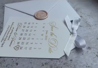 Video of a save the date calendar card with foil lettering and a satin ribbon, personalized wedding save the date tag with an envelope.