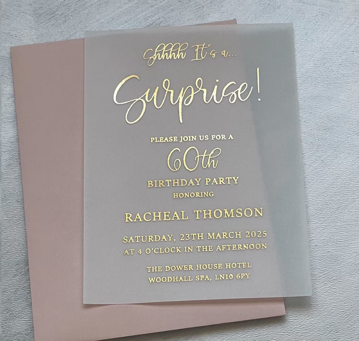 Close-up of foil lettering on a surprise 60th birthday invitation, with the name, date and time printed on vellum.