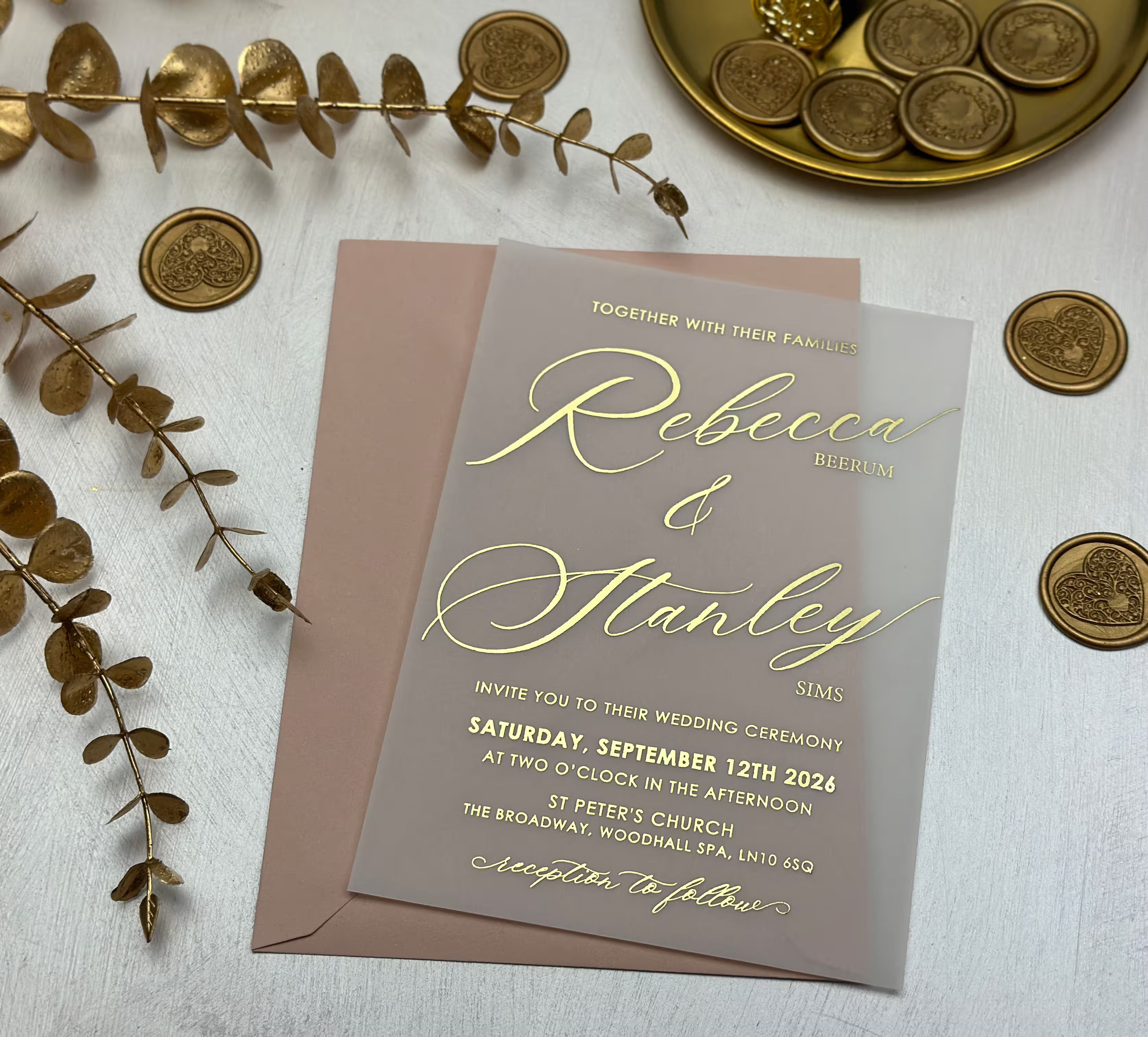 Close view of a vellum wedding invitation with gold foil script names and printed wedding details